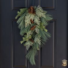 a wreath hanging on the front door of a house with pine cones and evergreen needles