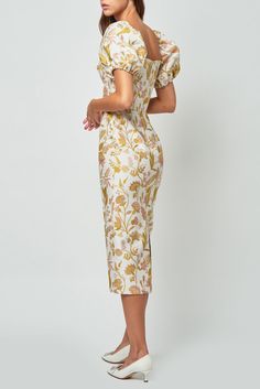 a woman in a white and yellow floral print dress with her hands on her hips