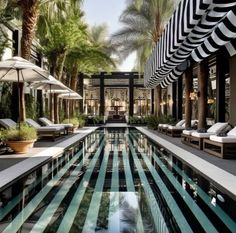 an outdoor swimming pool with lounge chairs and umbrellas next to it, surrounded by palm trees