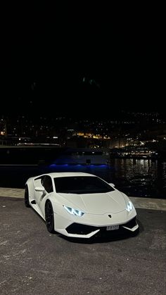 a white sports car parked in front of a body of water at night with the lights on