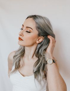 a woman with long gray hair wearing a white dress and holding her hand up to her ear