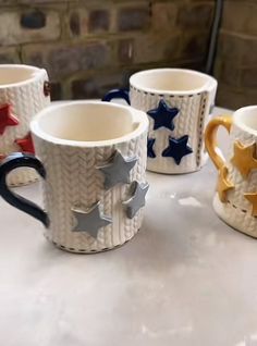 four coffee mugs with stars on them are sitting on a white counter top and one has gold, silver, and blue handles