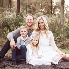 a family sitting on a blanket in the woods posing for a photo with their two children