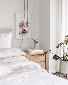 a bed with white sheets and pillows next to a potted plant on the nightstand