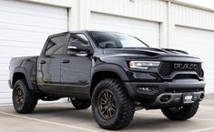 a black ram truck parked in front of a garage door with its hood up and wheels down