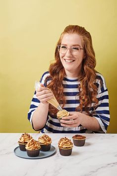 a woman sitting at a table with cupcakes in front of her and holding a spoon