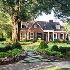 a large house surrounded by lush green trees and flowers in the front yard, with stone walkway leading up to it