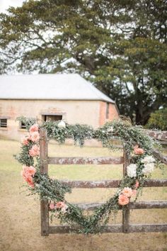 a wooden fence with flowers and greenery on it in front of an old barn