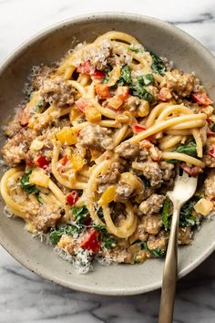 a bowl full of pasta with meat, spinach and cheese on it next to a fork