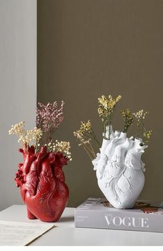 two vases with flowers in them sitting on a table next to a book,