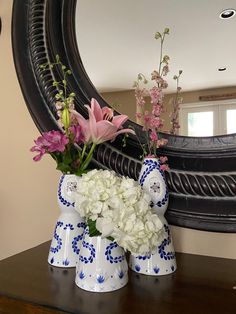 two white and blue vases with flowers on a table in front of a mirror