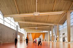 several people are walking in an open space with orange and white wall panels on the ceiling