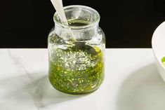 a glass jar filled with green liquid next to a white bowl full of food on a table