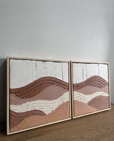 two wooden paintings are sitting on a table next to each other, one is brown and the other is white