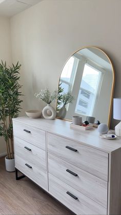 a white dresser topped with a mirror next to a potted plant