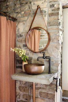 a bathroom with stone walls and a round mirror on the wall above a sink that is next to a shower curtain