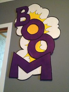 an image of the word boo spelled in purple and yellow on a gray wall with white clouds above it