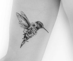 a small hummingbird with flowers on its back leg tattoo by the talented artist jane