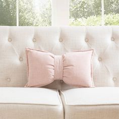 a white couch with two pink pillows on it and a window in the back ground