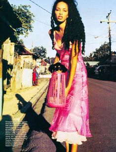 a woman in a pink dress is holding a birdcage on the side of the road