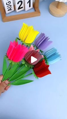 a person is holding some colorful flowers in front of a table with calendars on it