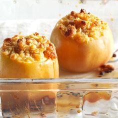 two baked apples with crumbled toppings sit in a glass dish