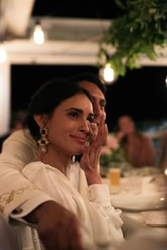 two people sitting at a table with food in front of them and one woman holding her hand up to her face