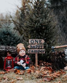 a little boy sitting next to a sign that says one happy camper