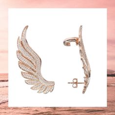 two pairs of earrings with wings on them in front of the ocean and pink sky