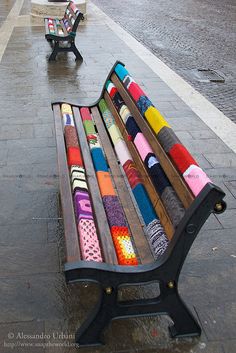 two benches with colorful scarves on them sitting next to each other in the rain