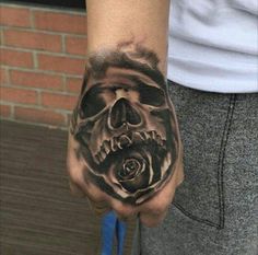 a hand with a skull and rose tattoo on it