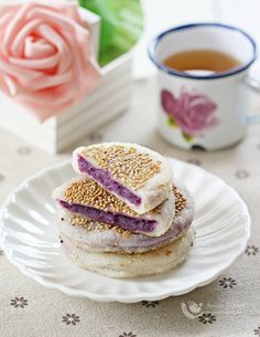 three sandwiches on a white plate next to a cup of tea and pink rose flowers