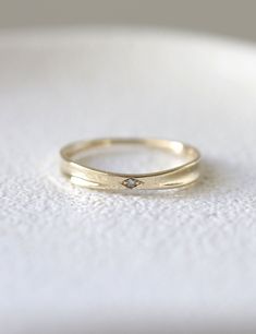 a yellow gold wedding band with a diamond set in the middle on a white surface