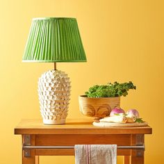 a green lamp sitting on top of a wooden table next to a potted plant