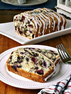 a loaf of blueberry bread on a white plate with a fork next to it