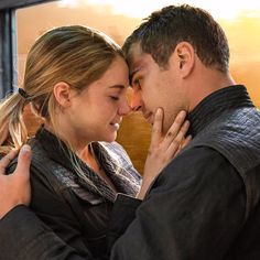 a man and woman standing next to each other in front of a window looking at each other