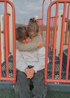 two people sitting on a playground with their arms around each other