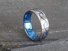 a blue and silver wedding ring with waves on the inside is sitting on a rock