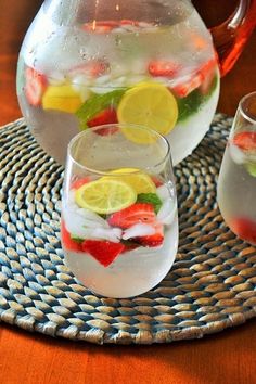 two glasses filled with water, lemons and strawberries on top of a woven place mat