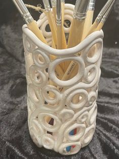 a white cup with pens and pencils in it