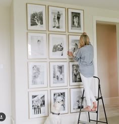 a woman standing on a ladder in front of a wall full of pictures and a dog