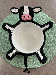 a small black and white cow sitting in front of a bowl on top of a green place mat