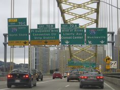 cars are driving on the highway in front of some tall buildings and traffic signs above them