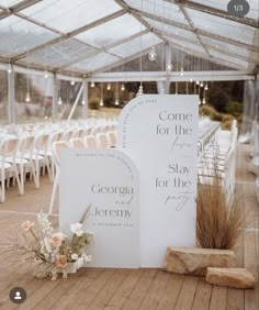 two white signs sitting on top of a wooden floor next to chairs and flowers in vases