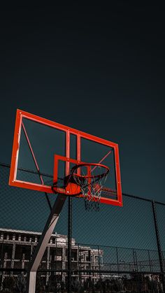 an orange basketball hoop in front of a chain link fence with a building in the background