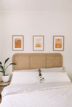 a bed with white linens and two framed pictures on the wall above it, along with a potted plant