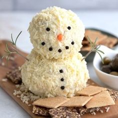 a snowman made out of rice sitting on top of a cutting board next to crackers and olives