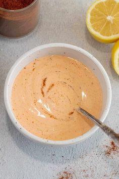 a white bowl filled with sauce next to some sliced lemons and cinnamon on a table