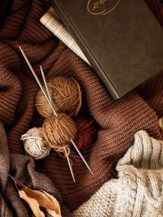 yarn and knitting needles are laying next to a book on a bed with a blanket