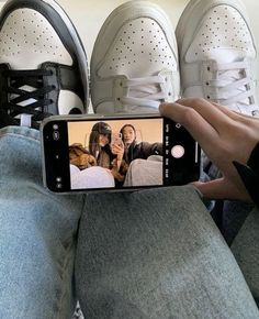 a person taking a selfie with their cell phone in front of two pairs of shoes